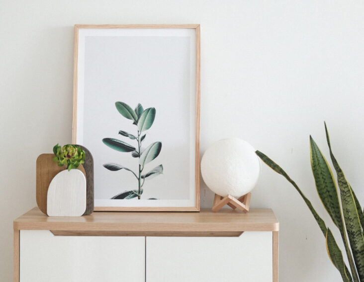 Modern white and brown wooden drawer with a wooden picture frame, stylish vase and ball shaped lamp on top