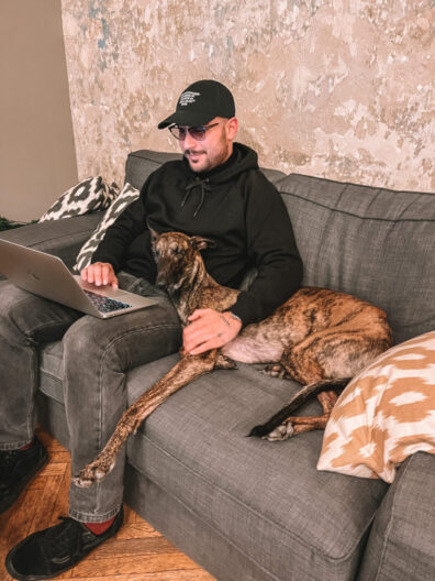 WFN project manager Ben sitting on a couch with a dog while working on web development projects on his laptop