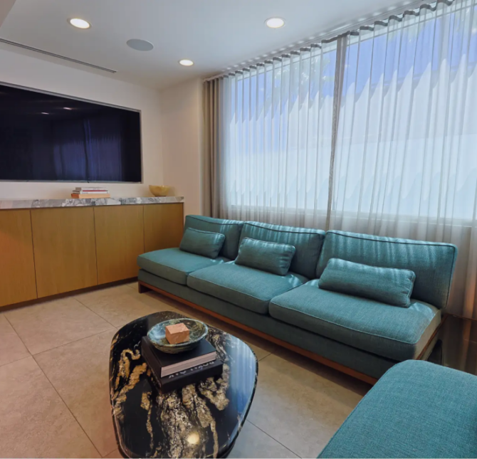 A cozy waiting lounge at Gramercy Center with plush blue sofas, a sleek marble coffee table, and natural light filtering through elegant curtains.